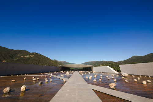 Exterior sloping plaza rocks  footpath water mountains  blue sky architecture