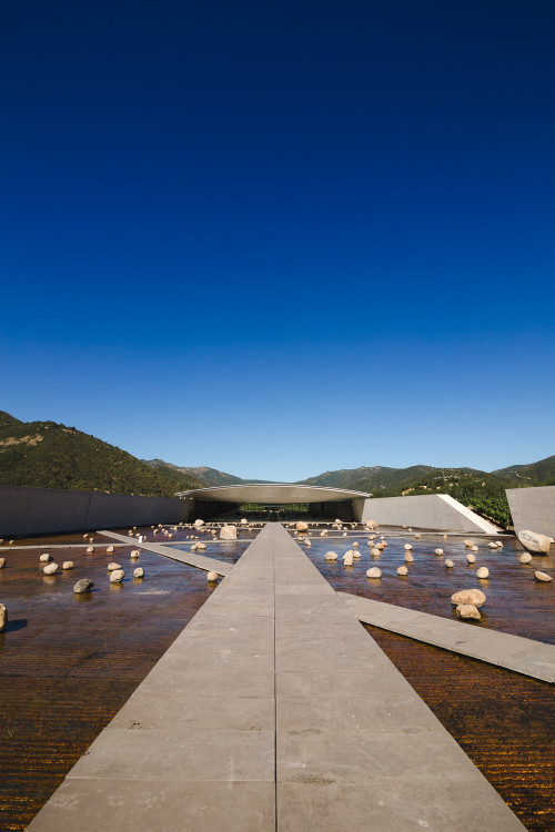 Exterior sloping plaza rocks  footpath water mountains  blue sky architecture