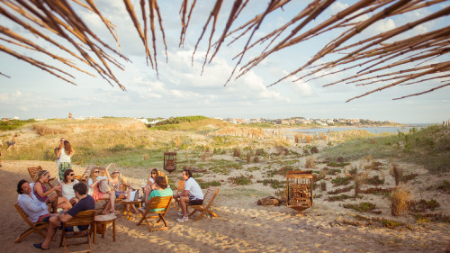 La Susana Restaurant José Ignacio Uruguay landscape sea beach bush sand  exterior houses people village blue sky clouds chair table group men women brazier firewood roof glass bottle ice bucket