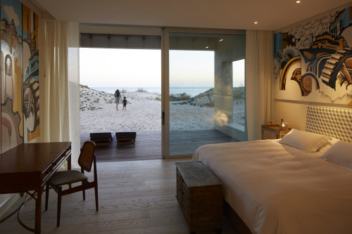 Bahía VIK José Ignacio Conde Suite  Duna Bungalow sand bush interior bedroom double bed headboard pillows night table lamps desk chair bench paintings curtains woman child light Lounging chairs sea