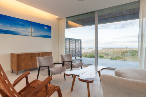 Bahía VIK José Ignacio Vidrio Arena Bungalow living  room sofas chair table window view sea wood curtains furniture paintings 
rocking sand bush lights interior armchair