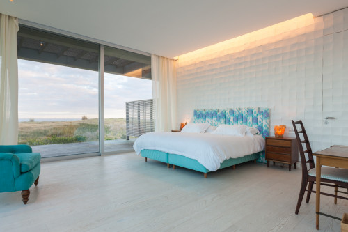 Bahía VIK José Ignacio Vidrio Notas Bungalow bedroom double bed headboard pillows night table lamps armchair chair desk door window view curtains sea sand bush landscape interior