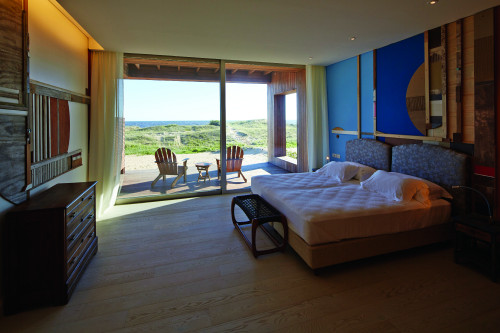 Bahía VIK José Ignacio Pepe Suite Madera Bungalow bedroom double bed headboard pillows night table lamps curtains paintings bench Chest of drawers furniture window view sand bush sea sculpture wood interior